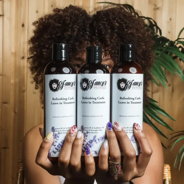 Three bottles of Fancy's Hair Innovation Refreshing Curls Leave in Treatment held in front of a woman's face.